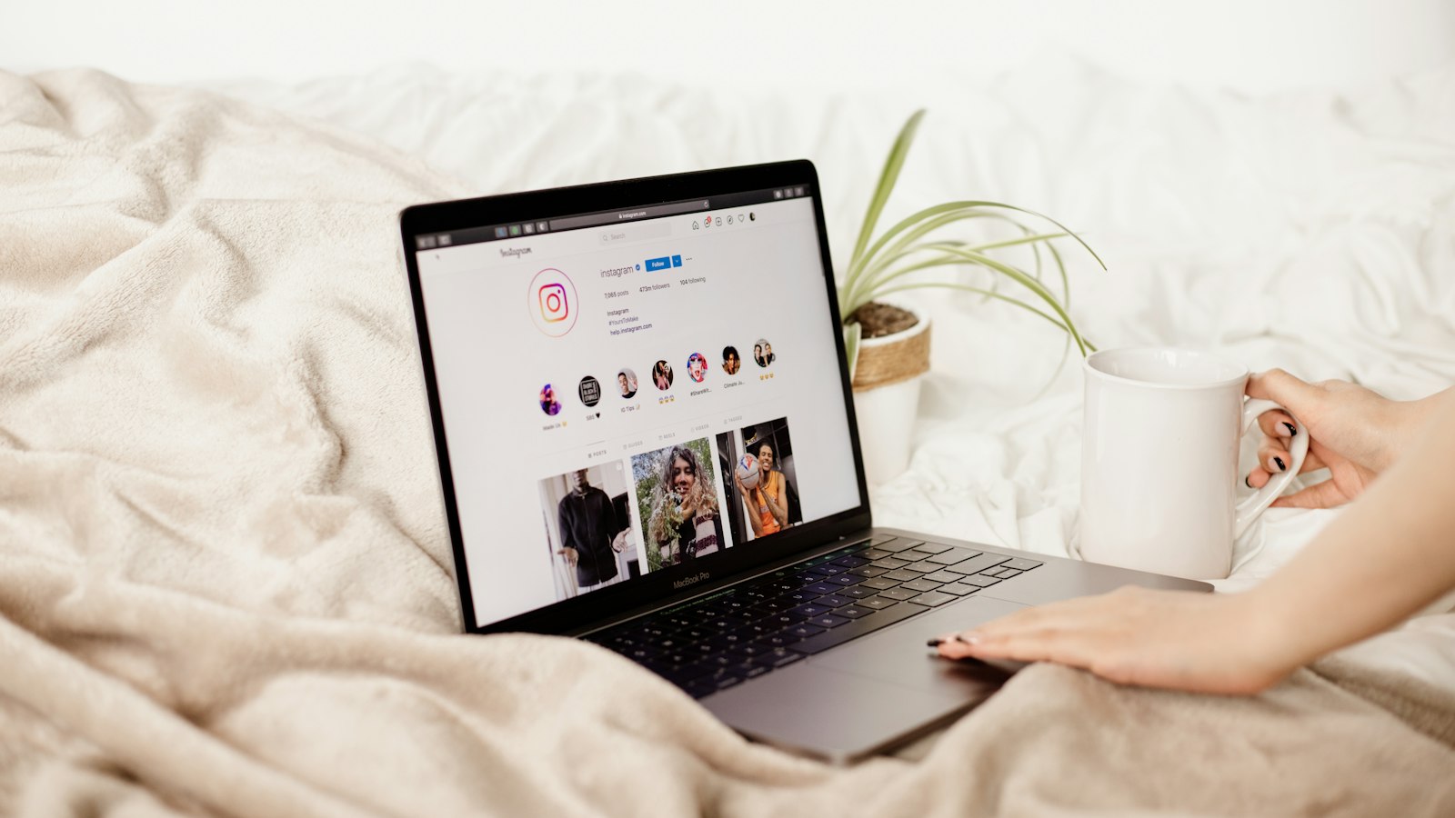a woman is holding a coffee cup and looking at her laptop