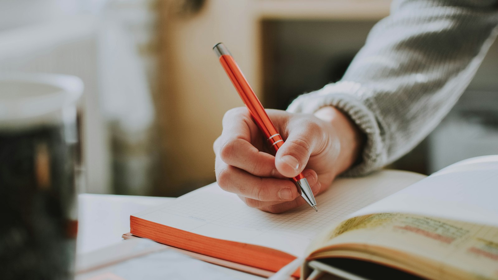 person holding on red pen while writing on book