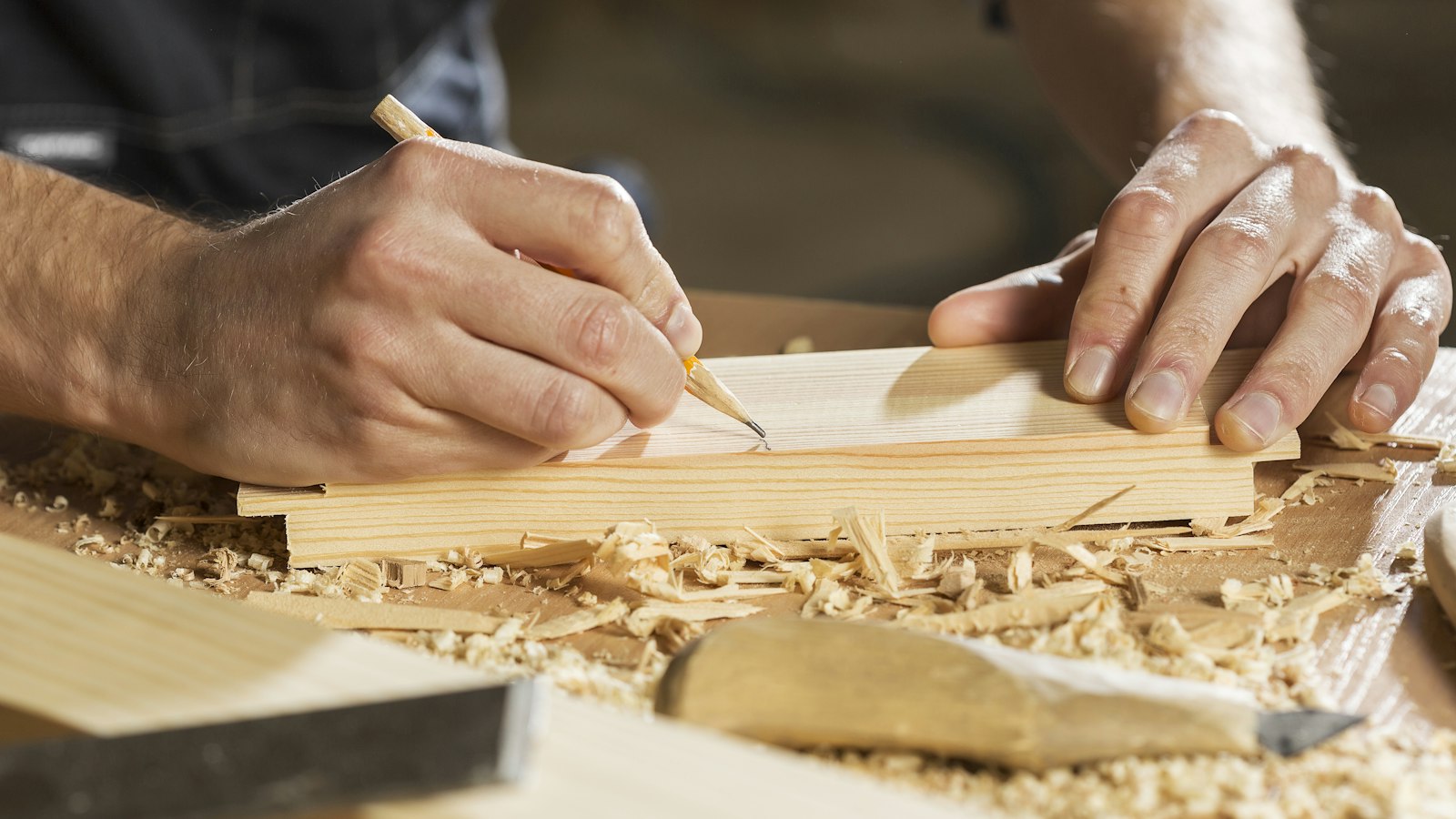 A person marking a line on a wooden board with a pencil