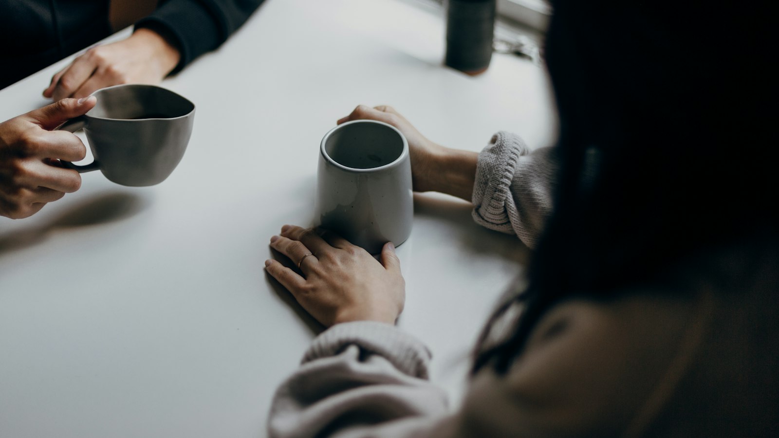 two people holding gray mugs at table