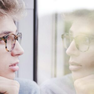 a man wearing glasses looking out a window