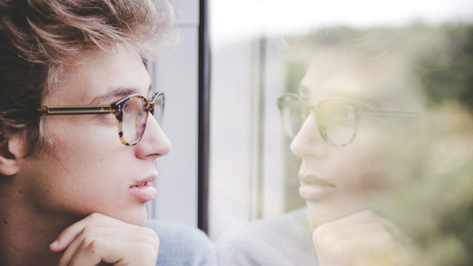 a man wearing glasses looking out a window