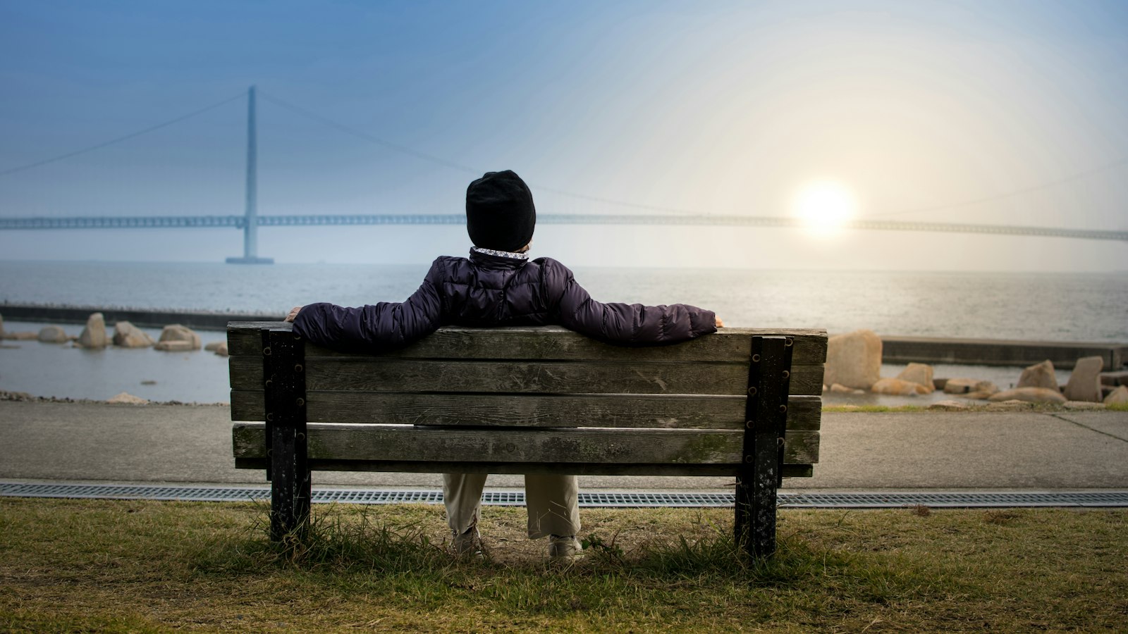 person sitting on bench facing suspension bridge
