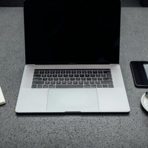 turned-off MacBook Pro between cup of coffee, iPhone, notebook, and pen