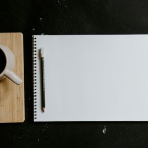 A cup of coffee and notebook with pen on desk