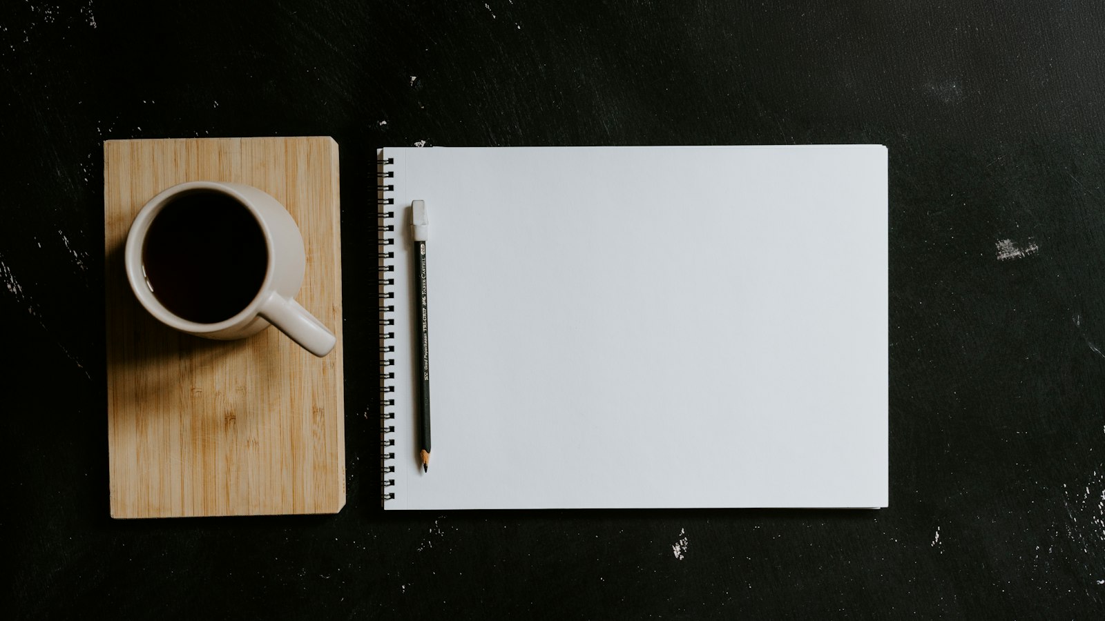 A cup of coffee and notebook with pen on desk