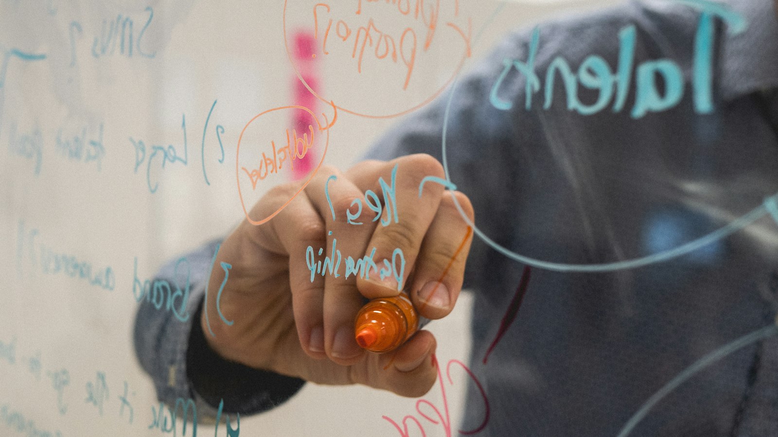 person writing on glass whiteboard with diagrams