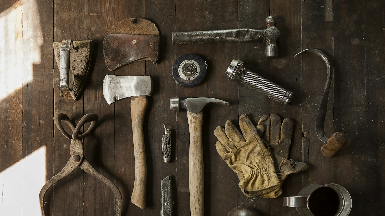 Vintage tools including an axe, hammer, gloves, and metal implements on dark wooden planks