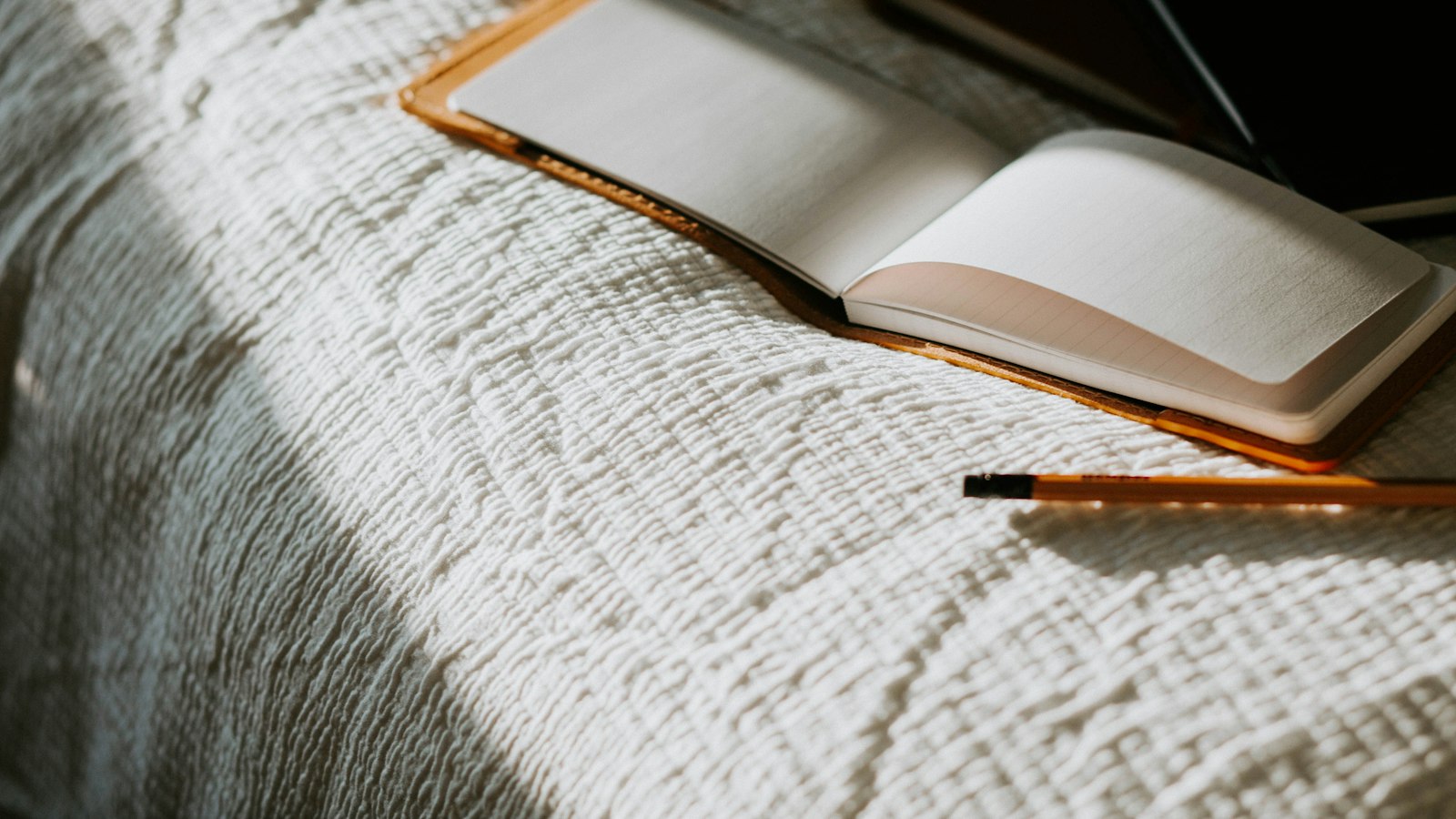 an open book sitting on top of a bed next to a pencil