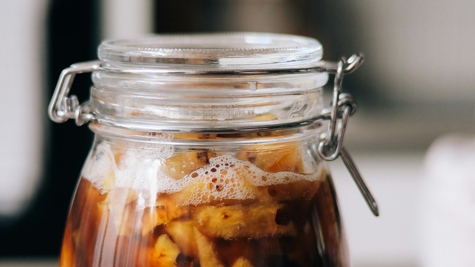 A clear glass jar containing brown liquid and floating ingredients