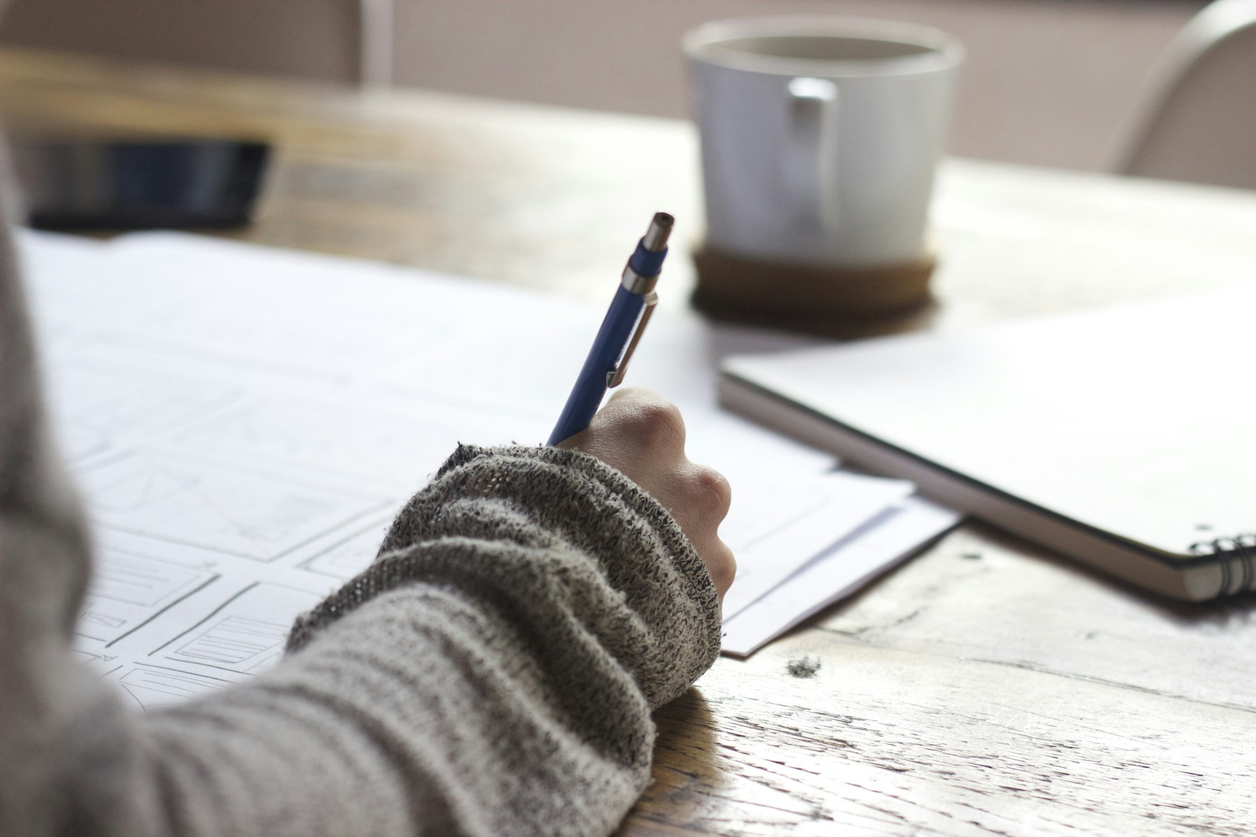 A person writing in a notebook beside a laptop