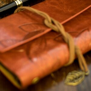a brown leather notebook with a pen on top of it