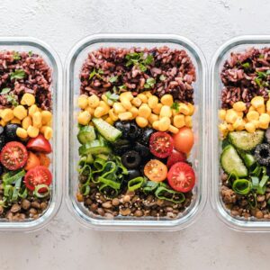 Three glass containers filled with rice, corn, olives, tomatoes, cucumbers, and lentils
