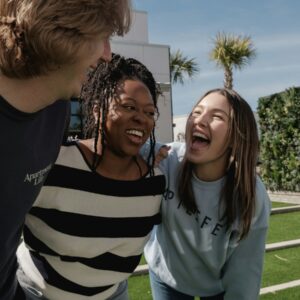 Three friends laughing together outdoors on a sunny day