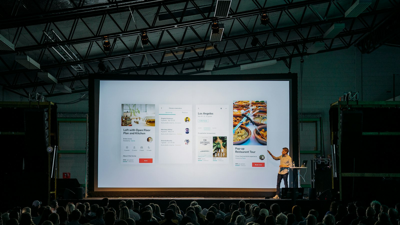 person discussing while standing in front of a large screen in front of people inside dim-lighted room