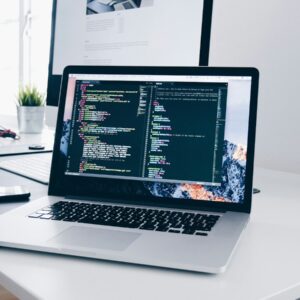A MacBook with lines of code on its screen on a busy desk
