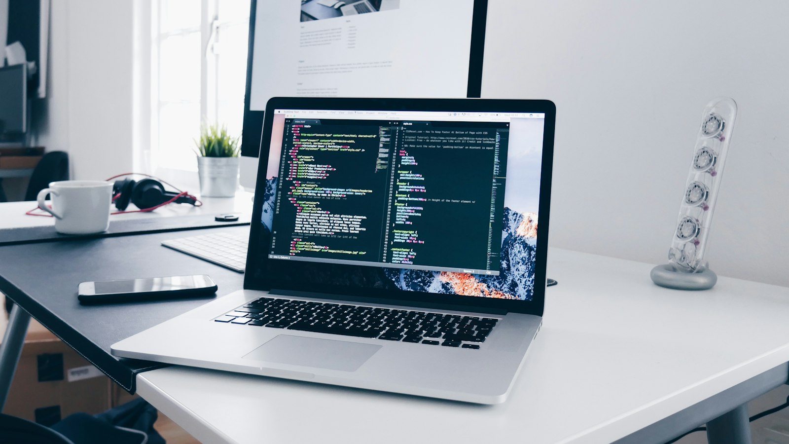 A MacBook with lines of code on its screen on a busy desk