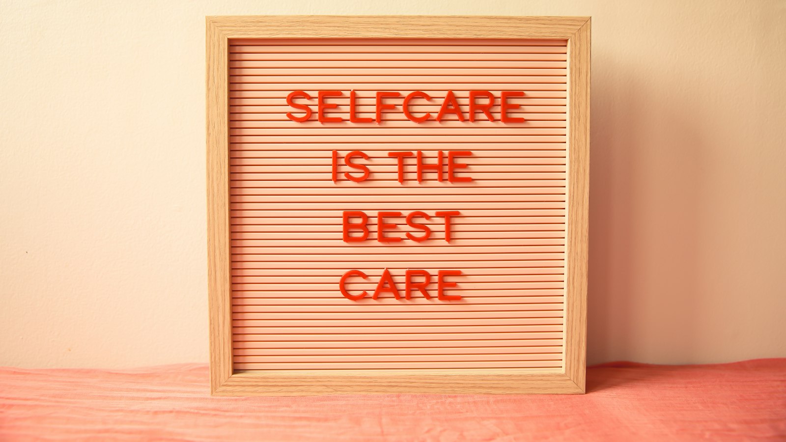 A wooden letter board with red text reading "SELFCARE IS THE BEST CARE"