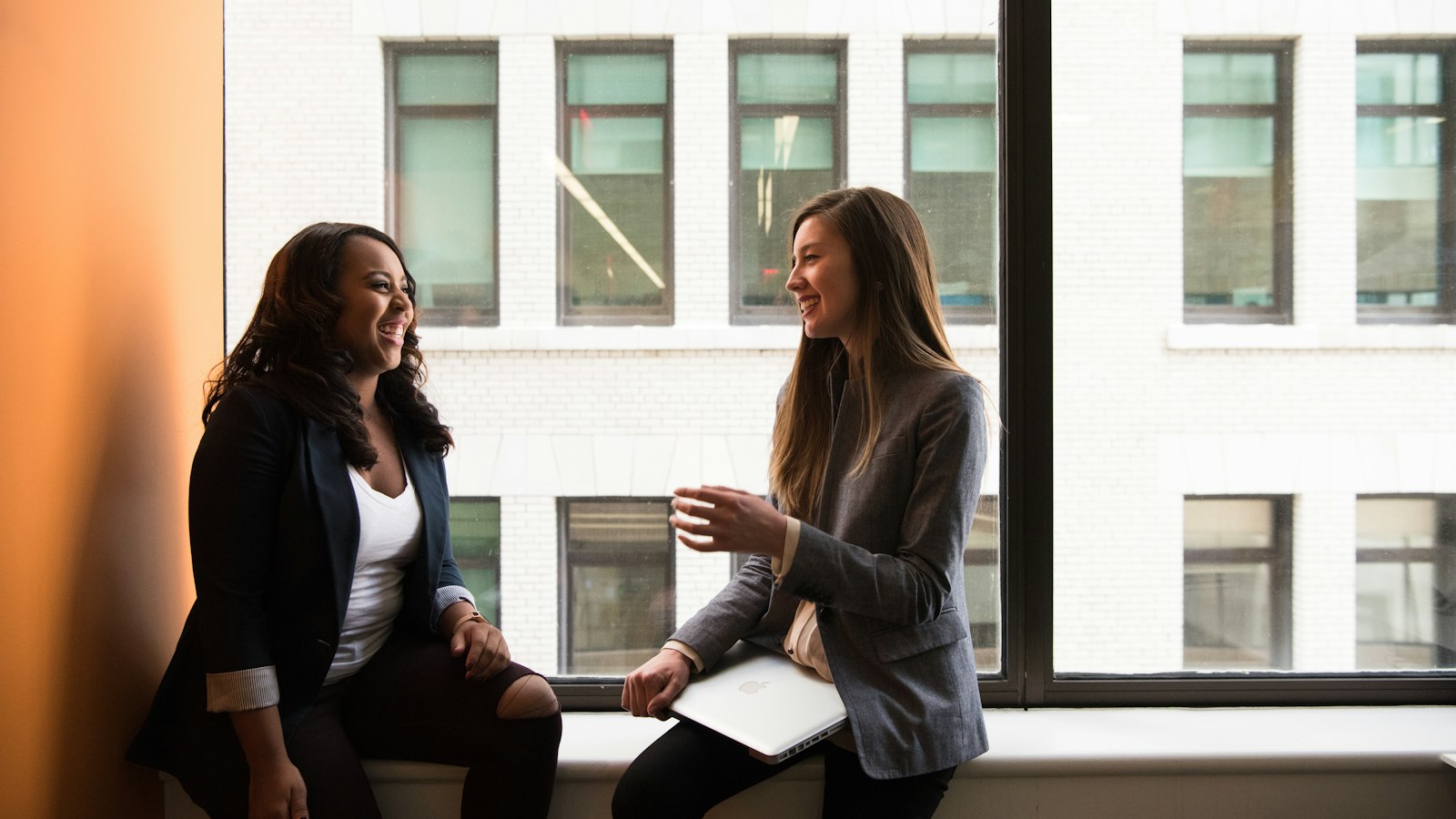two woman sitting by the window laughing