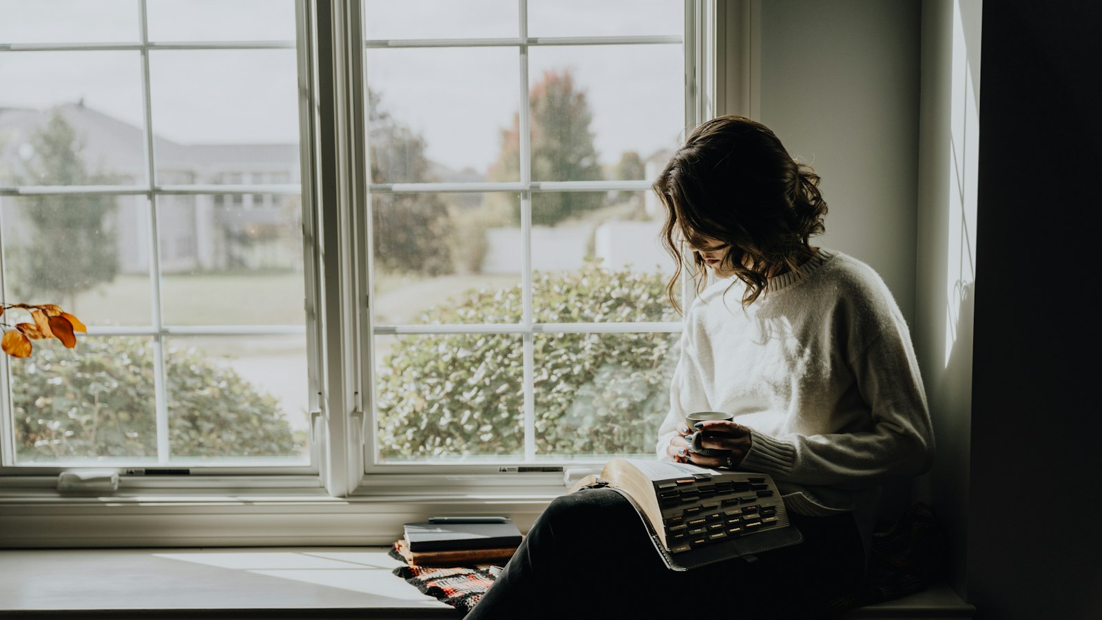 A woman in a white sweater holding a mug while reading a book