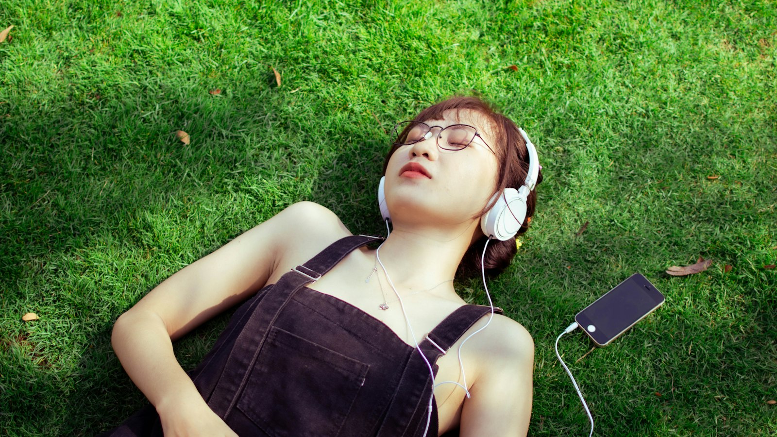 a woman laying on the grass listening to music