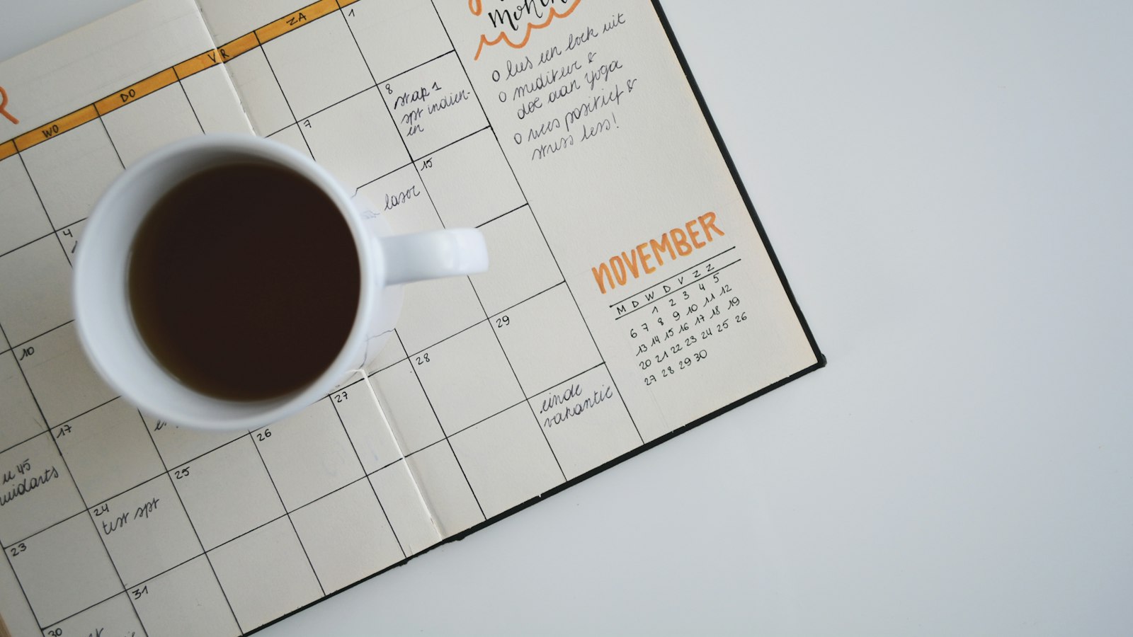 white ceramic mug with coffee on top of a planner