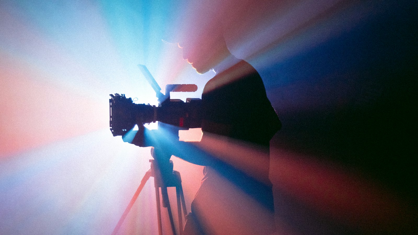 A person filming with a camera on a tripod in blue and red light