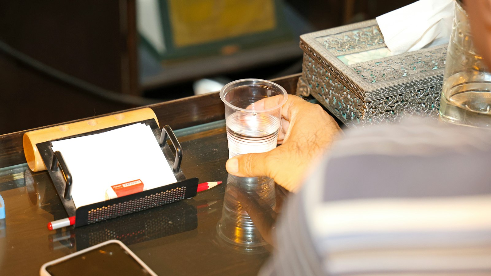 A person holding a plastic cup of water at a desk with stationery